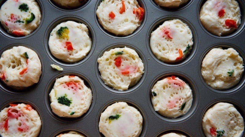 Fluffy white egg white bites in a muffin tin with visible flecks of red pepper and spinach, light and airy texture