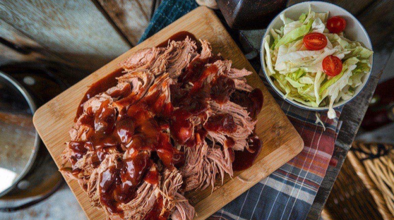 Slow cooker filled with tender shredded pulled pork in smoky BBQ sauce, with pulled pork sandwiches plated beside it