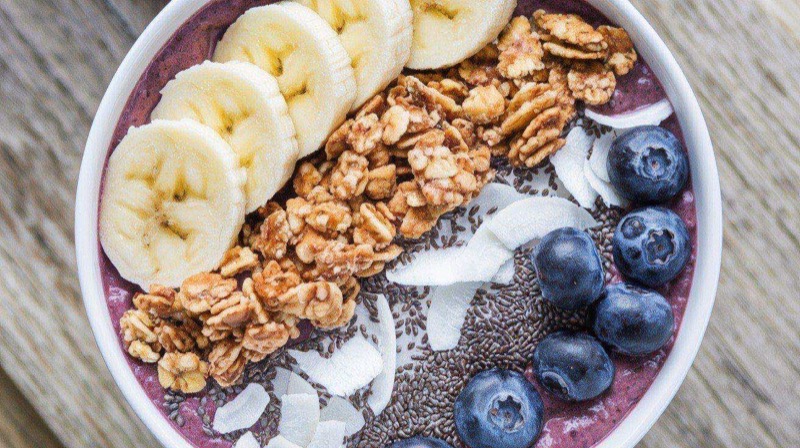 Two thick and creamy smoothie bowls topped with sliced banana, fresh berries, granola, coconut flakes, and chia seeds