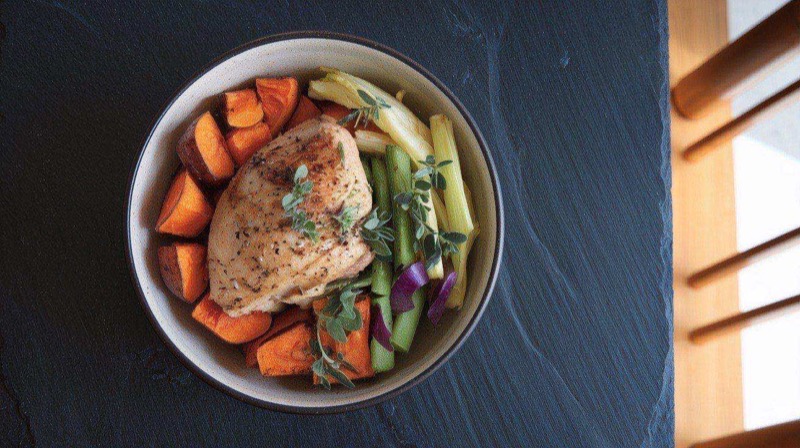 High-protein sweet potato chicken bowl with roasted orange cubes, sliced chicken breast, black beans, and green avocado crema