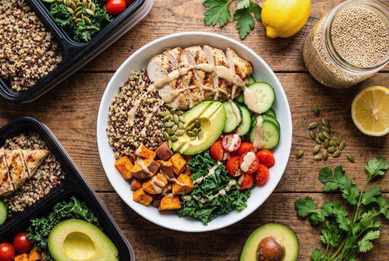 Meal prep bowl with sliced grilled chicken, fluffy quinoa, cherry tomatoes, cucumber, and tahini dressing