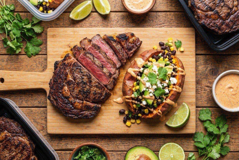 Sliced grilled New York strip steak next to a split sweet potato loaded with Greek yogurt and green onions