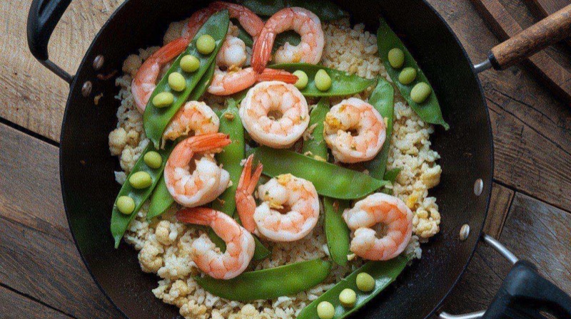 Sizzling shrimp stir fry with colorful snap peas, red bell pepper, and cauliflower rice in a wok, garnished with sesame seeds