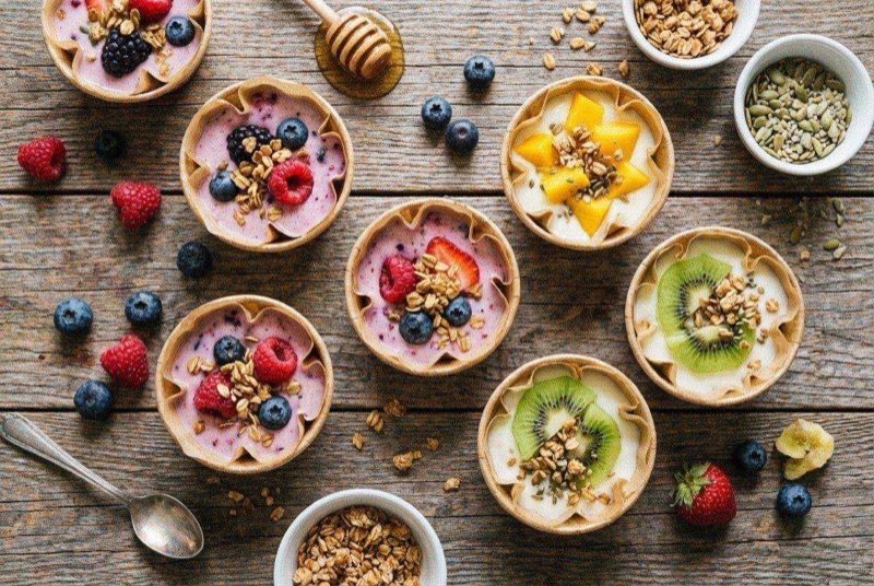 Colorful frozen yogurt cups topped with strawberry pieces, blueberries, and mango chunks in a silicone muffin tray