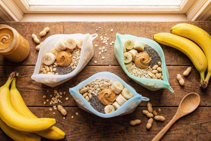 Five labeled zip-top freezer bags filled with banana slices, spinach, and smoothie ingredients laid flat on a cutting board