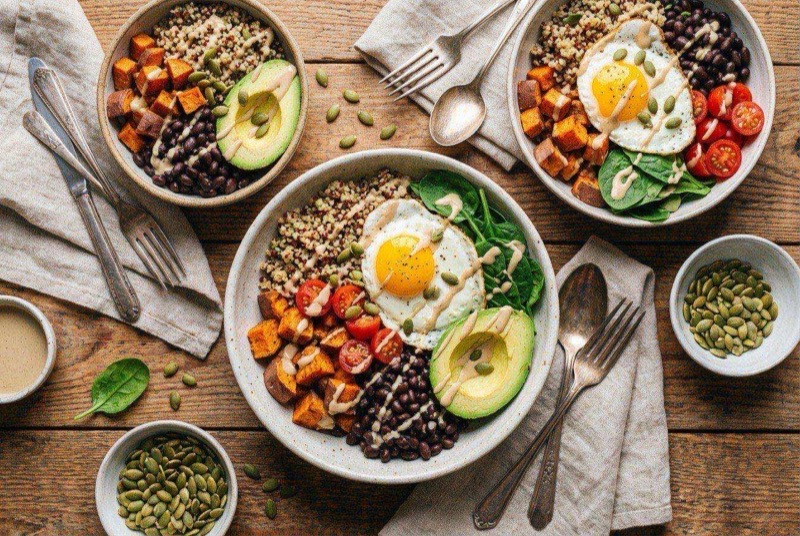 Meal prep bowl of fluffy quinoa topped with roasted zucchini, cherry tomatoes, red onion, and a drizzle of tahini