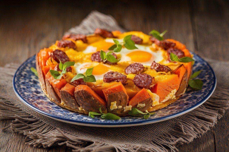 Sliced breakfast casserole with sweet potato base, sausage crumbles, and egg layers in a glass baking dish