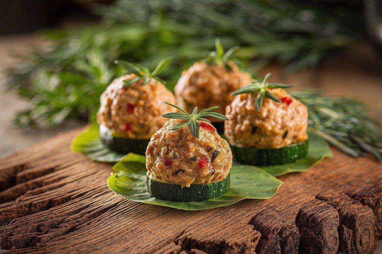 Rows of golden mini turkey zucchini meatballs on a parchment-lined baking sheet with a small bowl of marinara for dipping