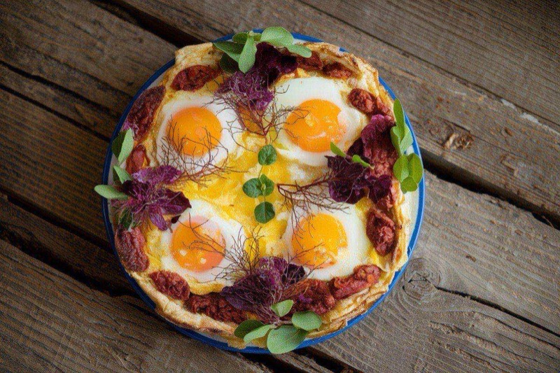 Sliced Mediterranean egg bake in a baking dish showing layers of spinach, feta, sun-dried tomatoes, and olives