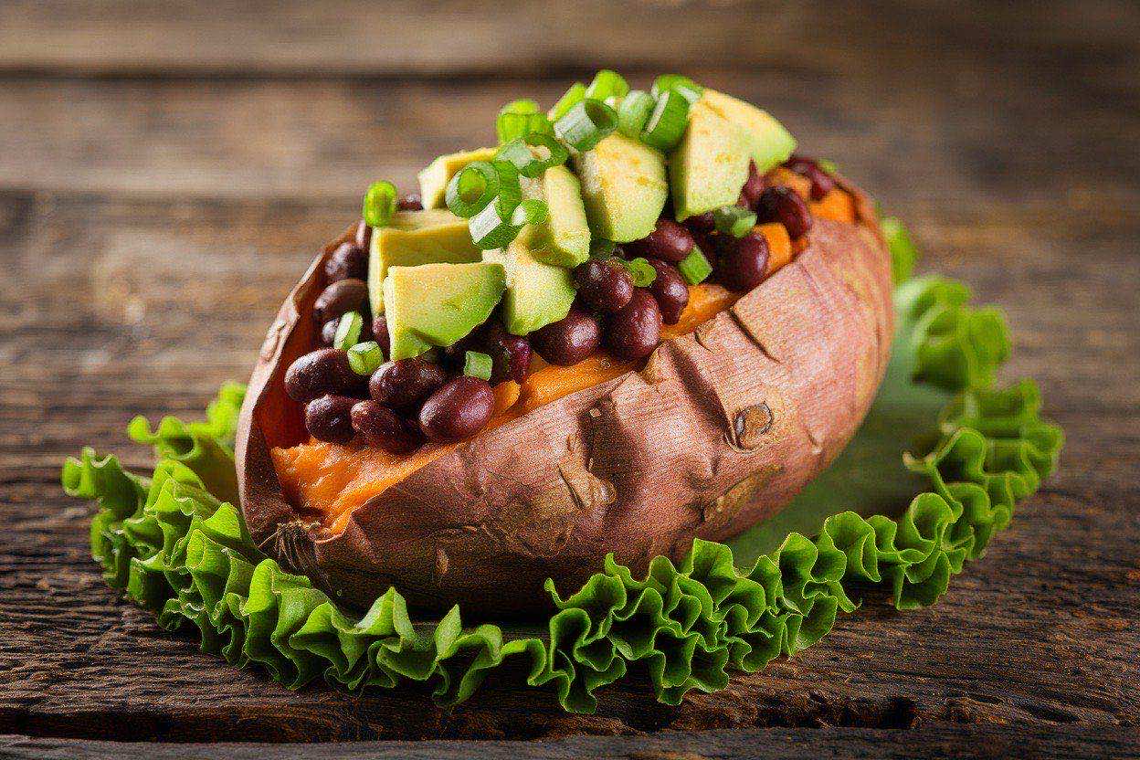 Split-open microwave-cooked sweet potato stuffed with seasoned black beans, diced avocado, and fresh cilantro